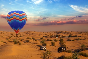 A hot air balloon floating over the safari with two vehicles on the safari