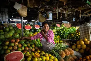 A woman smiling at a vibrant fruit stall in a market in Nairobi, Kenya