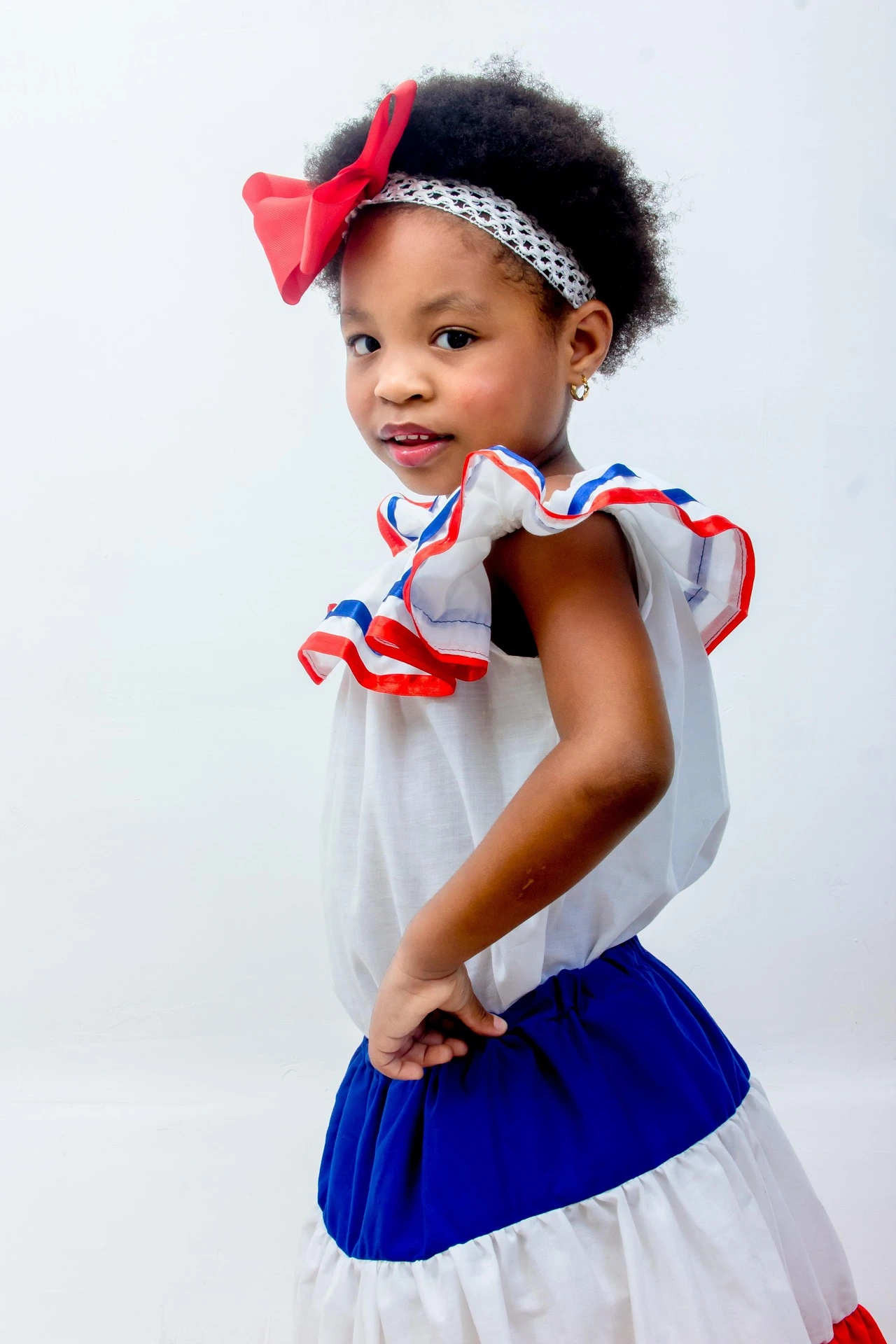 A young girl with an afro hairstyle wearing a red, white, and blue dress with a red bow in her hair