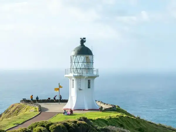 Gemini said A bright white lighthouse stands on a lush green headland overlooking the vast blue ocean under a clear sky.