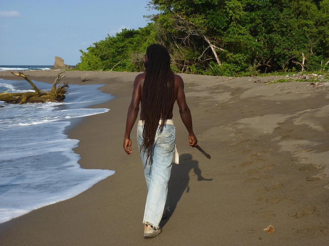 Person with dreadlocks walking along a beach in Jamaica featured