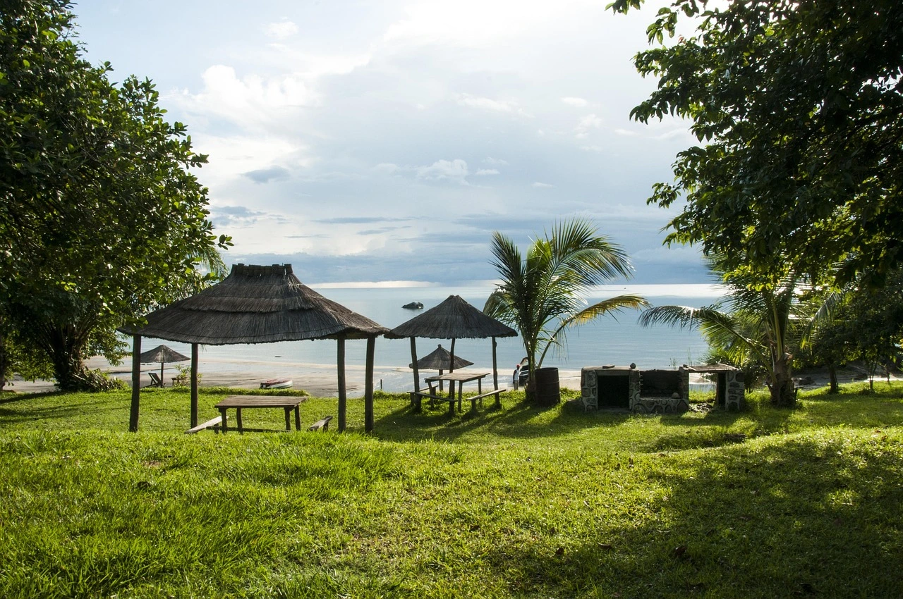 Thatched-roof huts and picnic tables on a grassy lawn by Lake Malawi featured