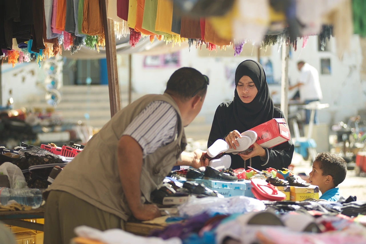 A woman in a black hijab holds up a pair of white sandals