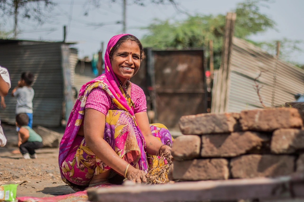 A woman is smiling while sitting on the ground in a rural setting in India featured