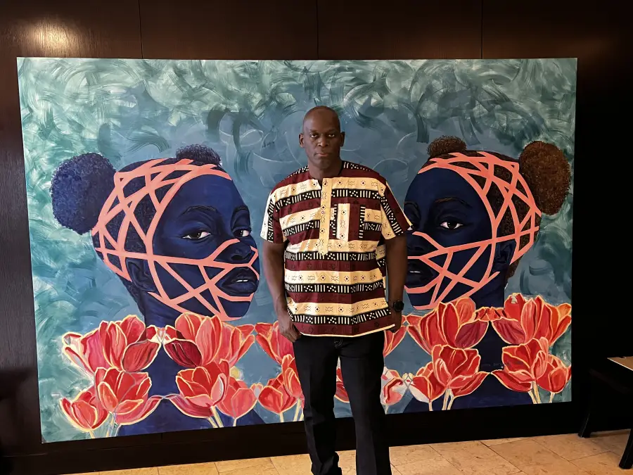 Martin stands before a large vibrant painting of two blue-toned figures with coral geometric patterns and red tulips.