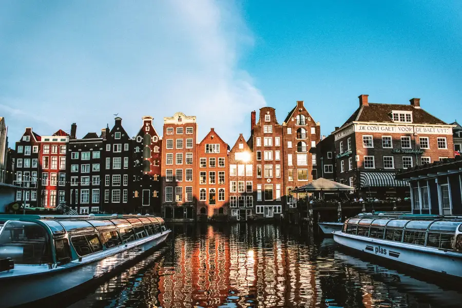 River cruise boats docked along Amsterdam's canal at golden hour; with iconic Dutch canal houses reflected in the water.
