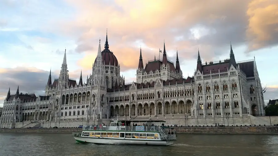 River cruise boat on the Danube passing the Hungarian Parliament Building in Budapest at sunset.