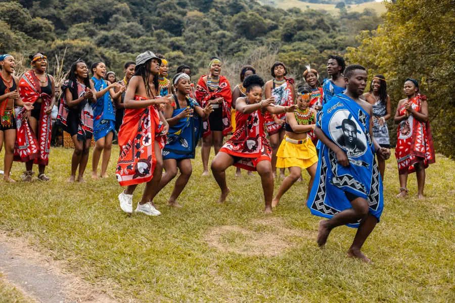 Group of young adults in vibrant traditional African attire performing a cultural dance outdoors on green grass; cruise-la...