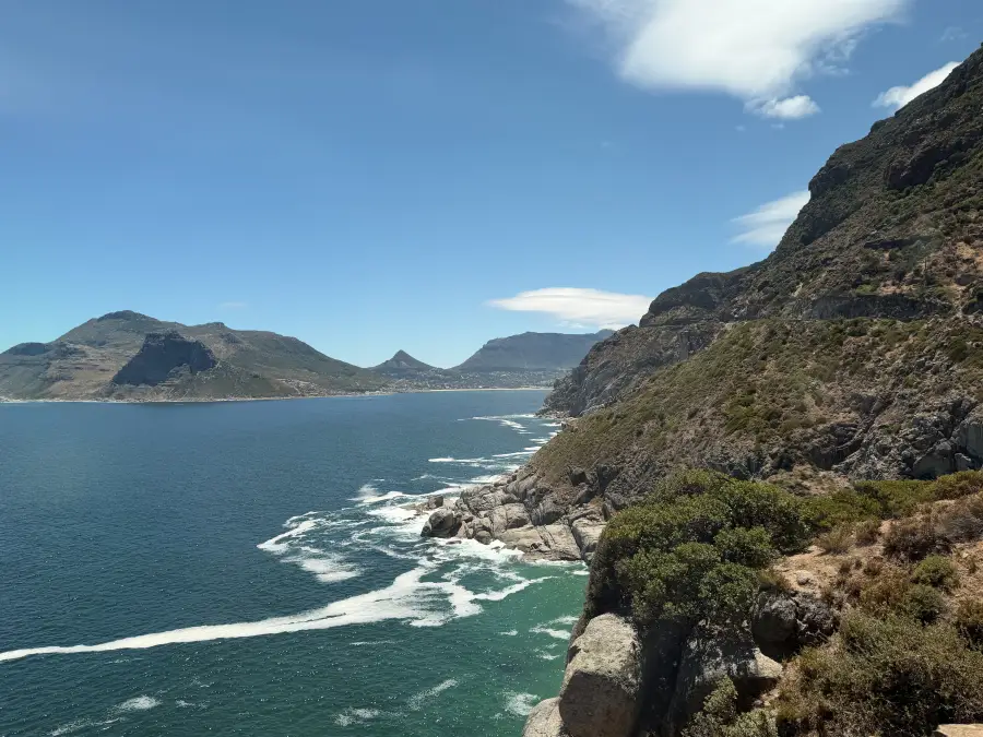 Dramatic rocky cliffs overlooking Hout Bay's turquoise waters with mountain backdrop; captured for eat-mea-2026 travel sho...