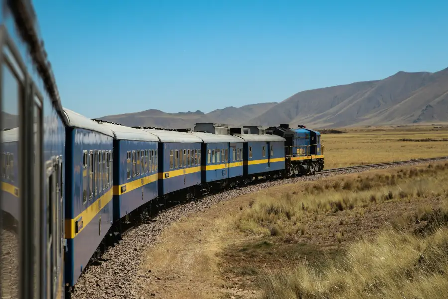 Blue and gold passenger train curves through Peru's high-altitude altiplano grasslands; evoking expedition-cruises style o...