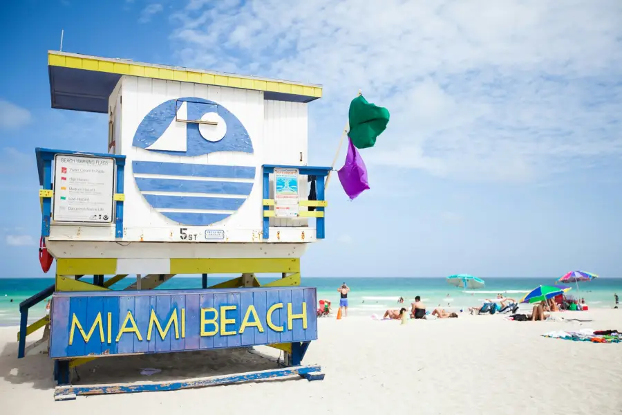 Colorful Miami Beach lifeguard station at 5th Street with green and purple warning flags flying on a sunny day.