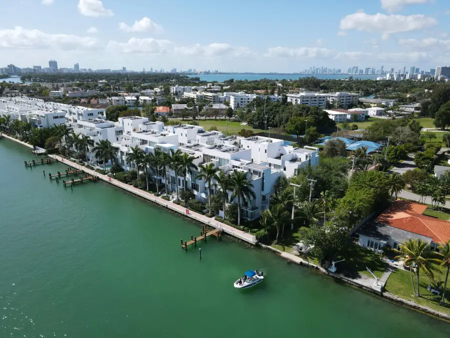 Aerial view of white modern waterfront condos along Miami Florida's Biscayne Bay with downtown skyline in background.