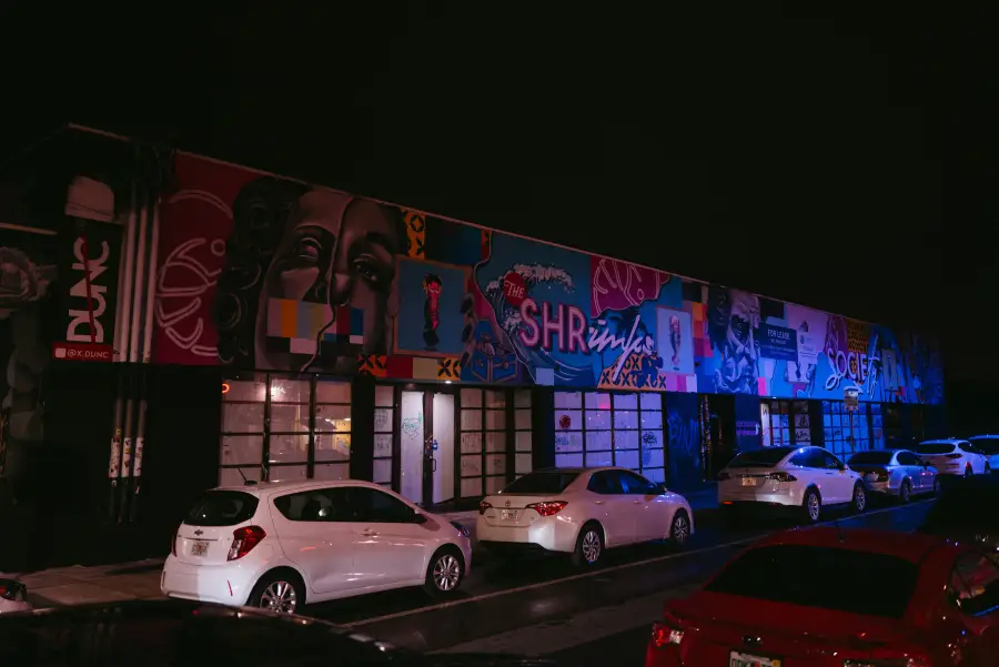 Colorful street murals illuminate a building facade at night in Miami; Florida's Wynwood arts district; with cars parked o...