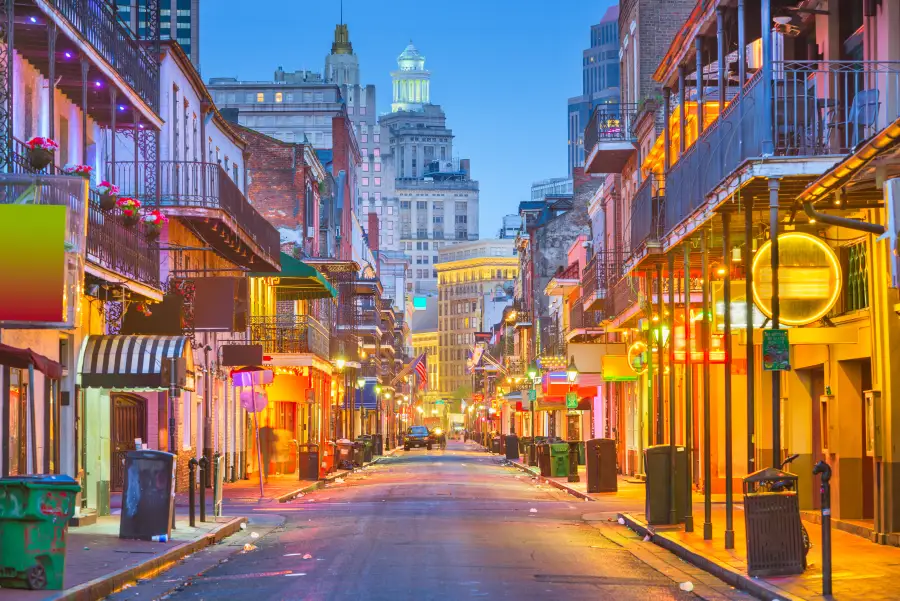 Bourbon Street in New Orleans Louisiana glows with colorful neon lights and iron-lace balconies at dusk with the city skyline beyond