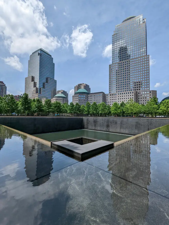 9/11 Memorial reflecting pool with cascading waterfall and Manhattan skyline in New York New York on a sunny day