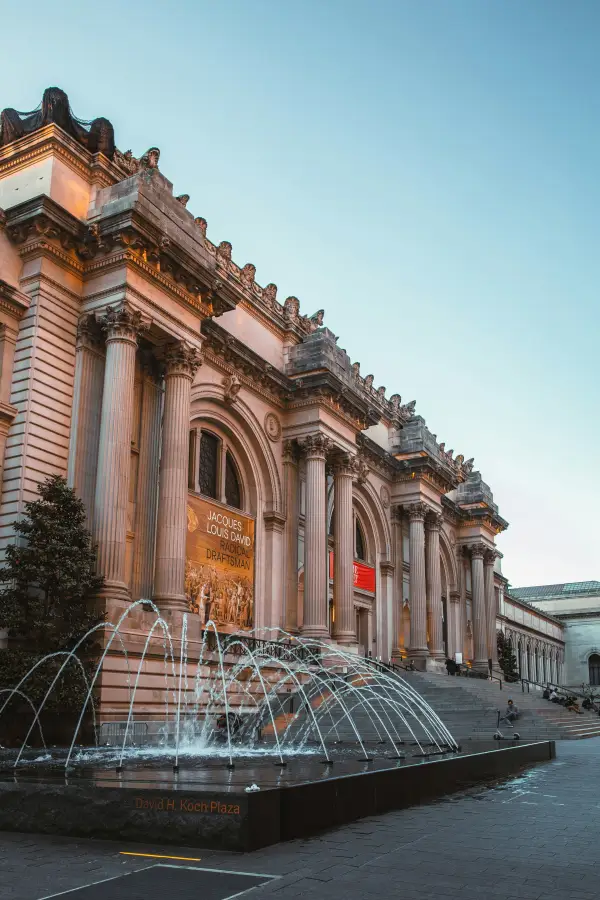 Metropolitan Museum of Art facade in New York New York with fountain at David H. Koch Plaza at dusk and Jacques-Louis David exhibition banner