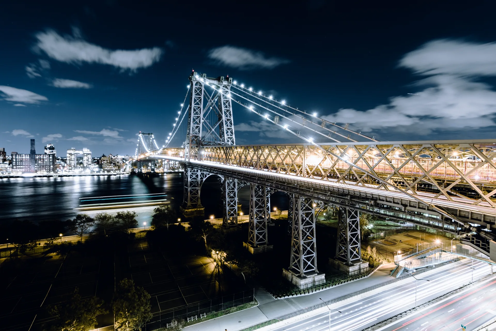 Williamsburg Bridge illuminated at night over the East River with the New York New York Manhattan skyline glowing in the background