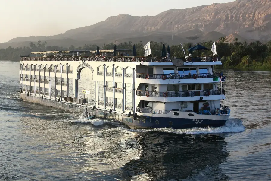 Large cruise-land riverboat sailing the Nile with desert cliffs and palm trees in the background; Egypt.