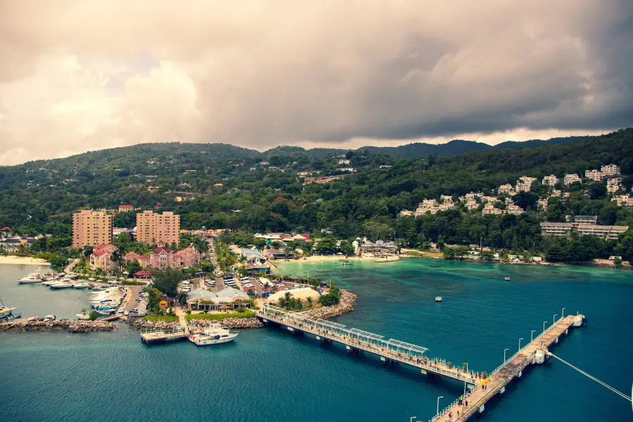 Aerial view of Ocho Rios Jamaica cruise port with turquoise bay pier marina and lush hillside town under stormy skies