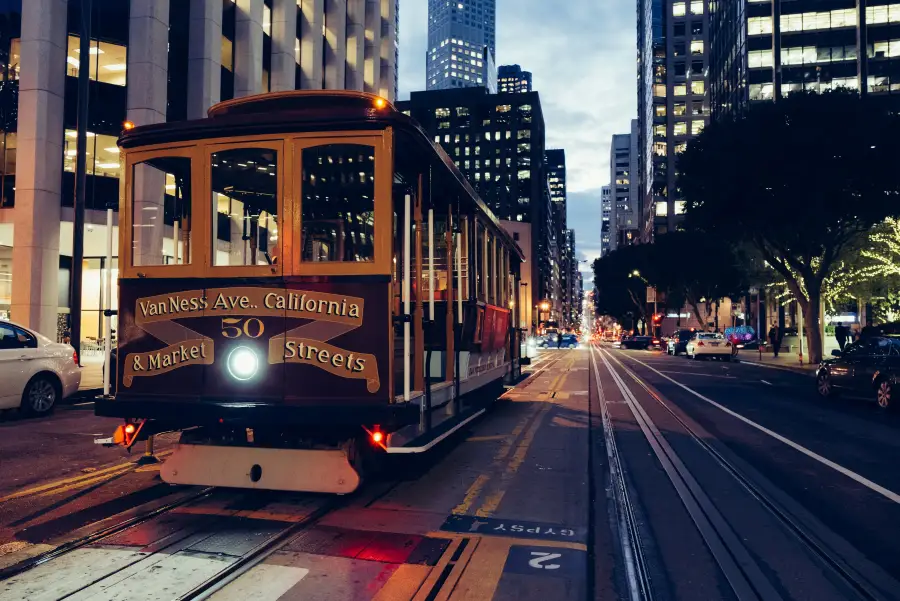 San Francisco CA cable car number 50 on California Street at dusk; with downtown skyscrapers and city lights in background.