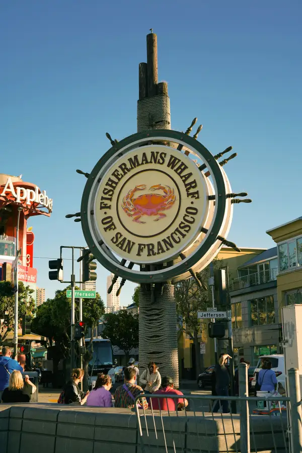 Iconic Fisherman's Wharf ship-wheel sign with crab emblem on Jefferson Street in San Francisco; CA; surrounded by visitors.
