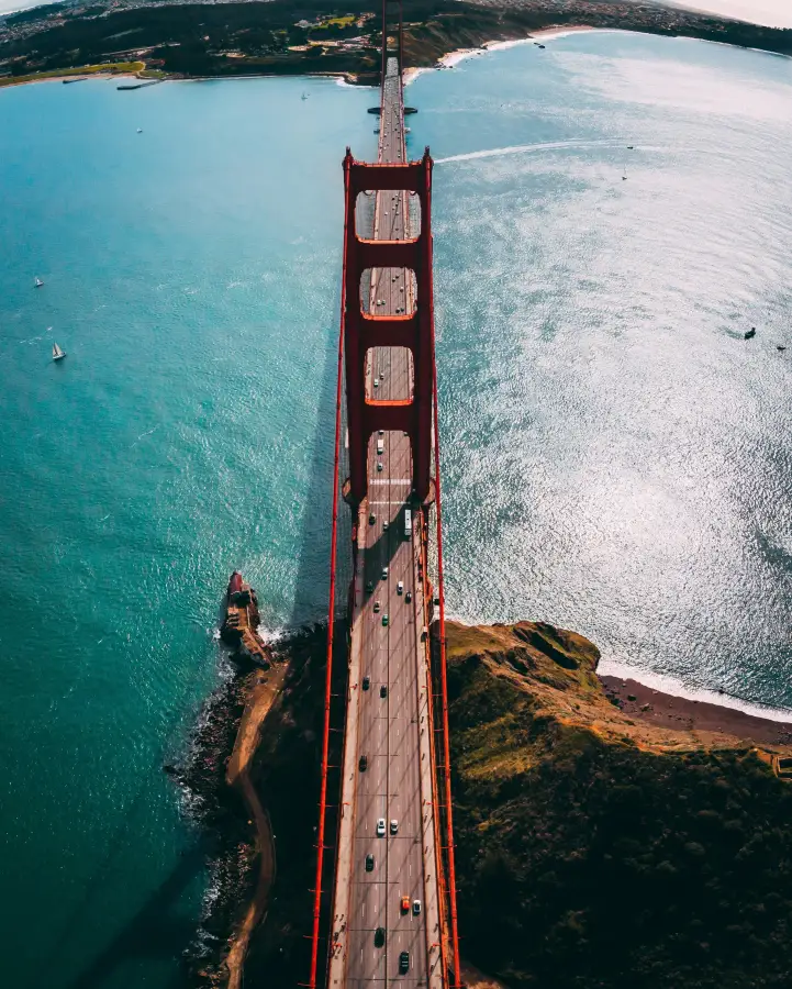 Aerial view looking down the Golden Gate Bridge in San Francisco; CA; with turquoise bay waters and light traffic below.