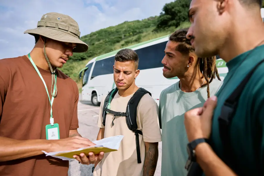 Travel support coordinator reviews documents with three travelers beside a coach bus during a group departure.