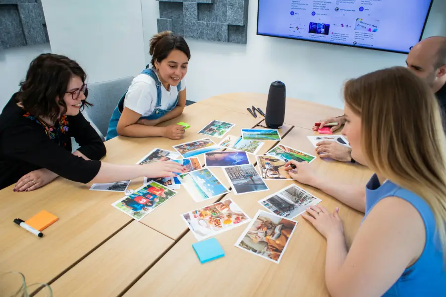 Four colleagues reviewing printed travel photos on a conference table during a travel-support planning session in a modern...