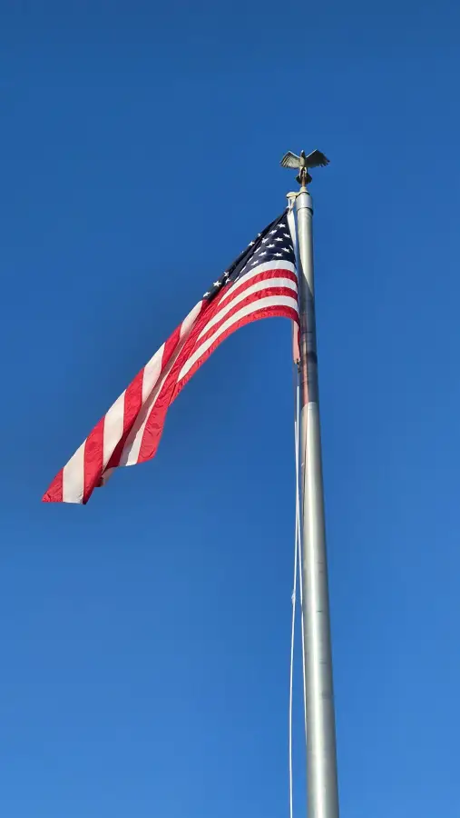 American flag waving from a flagpole against a clear blue sky for the America250 anniversary.