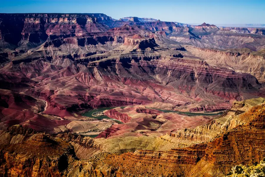 Aerial view of the Grand Canyon with the Colorado River winding through layered red rock formations.