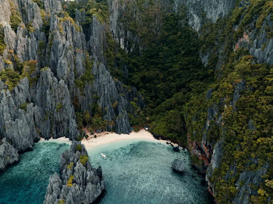 Aerial view of a secluded white-sand beach between towering limestone cliffs and turquoise water.