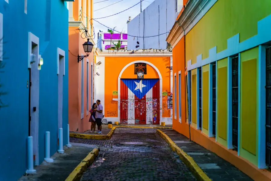 Cobblestone alley of colorful colonial buildings in Old San Juan with a Puerto Rican flag mural.