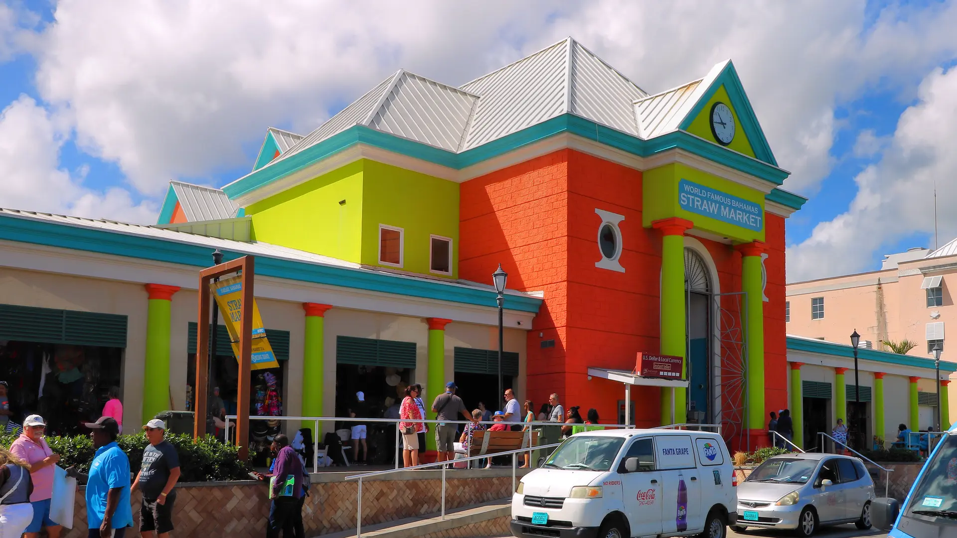 Shoppers outside the brightly painted Straw Market building in Nassau, The Bahamas, on a sunny day.