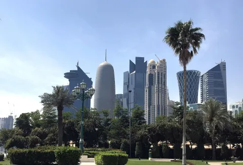 The West Bay skyline of Doha rising behind palm trees and parkland.