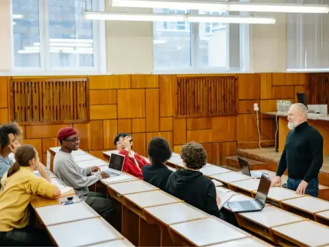 A classroom scene where a lecturer engages students seated with laptops in a modern lecture hall