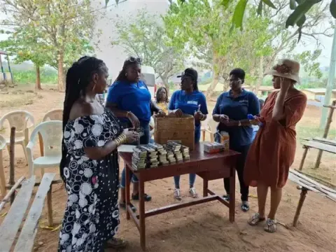 A group of people gathered around a wooden table outdoors are organizing or distributing stacks of small boxed supplies