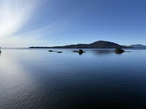 Calm blue waterway with small forested islets and a tree-covered hill in Alaska-Sitka's scenic island archipelago under cl...