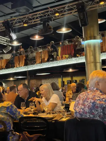 Guests dining at a lively multi-level restaurant in Cape Town; South Africa; with warm lighting and live musicians on the upper balcony.