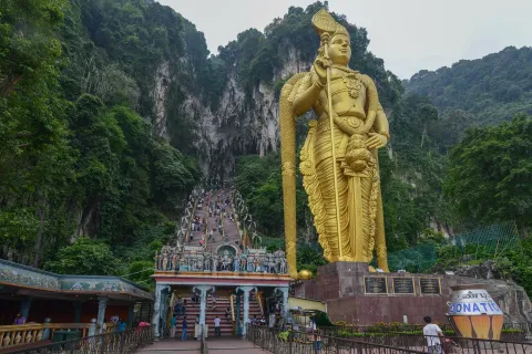 The gold Murugan statue beside the long stairway that climbs to the Batu Caves shrine near Kuala Lumpur.