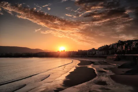 Low sun over La Concha bay at San Sebastian, Spain, the city curving around the shoreline behind the beach.
