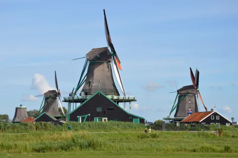 Timber windmills and green painted houses at Zaanse Schans in the Netherlands under a blue summer sky