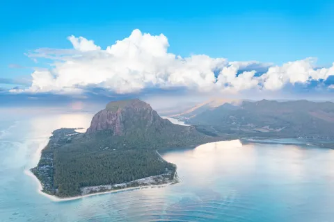 The Le Morne peninsula and its basalt mountain from the air, ringed by pale reef and turquoise lagoon, southwest Mauritius.