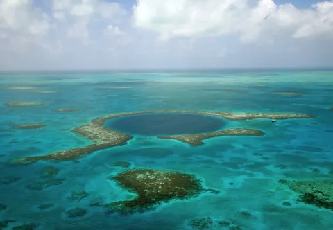 The dark circle of the Great Blue Hole ringed by reef in the turquoise shallows off Belize.