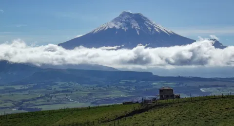 The snow capped cone of Cotopaxi rising above a band of cloud and green highland farmland in the Ecuadorian Andes