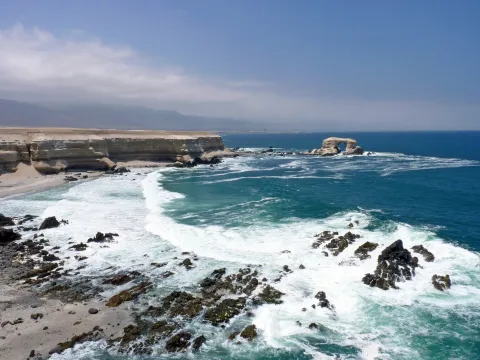 The La Portada sea arch offshore beyond surf and pale coastal cliffs on the Pacific coast near Antofagasta in Chile