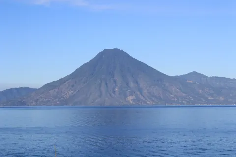 The blue water of Lake Atitlan in Guatemala with the wooded cone of Volcan San Pedro rising from the far shore