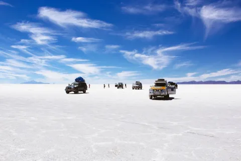 Four wheel drive vehicles and standing figures spread across the white salt crust of the Salar de Uyuni under a blue sky