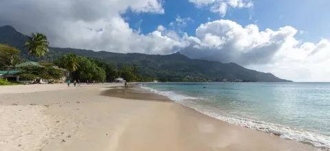 The curve of Beau Vallon bay on Mahé, pale sand meeting clear water with the forested Morne Seychellois range rising behind.