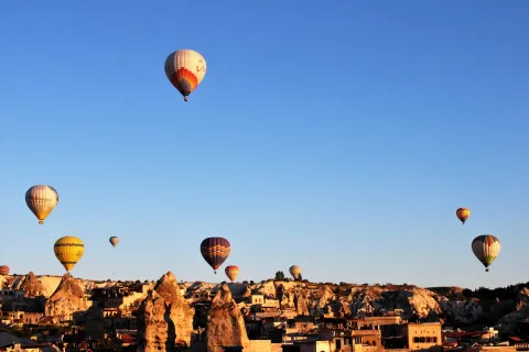Hot air balloons rising over the rock cones and carved valleys of Goreme in Cappadocia, Turkey, in early morning light.