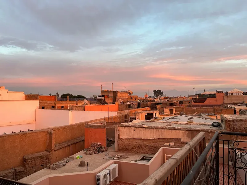 Flat clay rooftops of the Marrakesh medina under a pink and blue dusk sky.